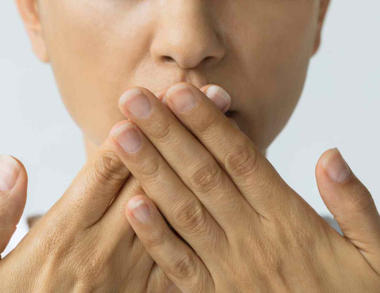 Ženska osoba prekriva usta rukama, simbolizujući težnju da ima sveže dah prirodnim metodama, ističući važnost diskretne brige o oralnoj higijeni