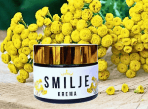 Smilje je najpoznatija i jedna od najdelotvornijih biljaka za postizanje mlade i negovane kože. Na slici se nalazi slika prirodne kreme od smilja u staklenoj ambalaži sa zlatnim poklopcem